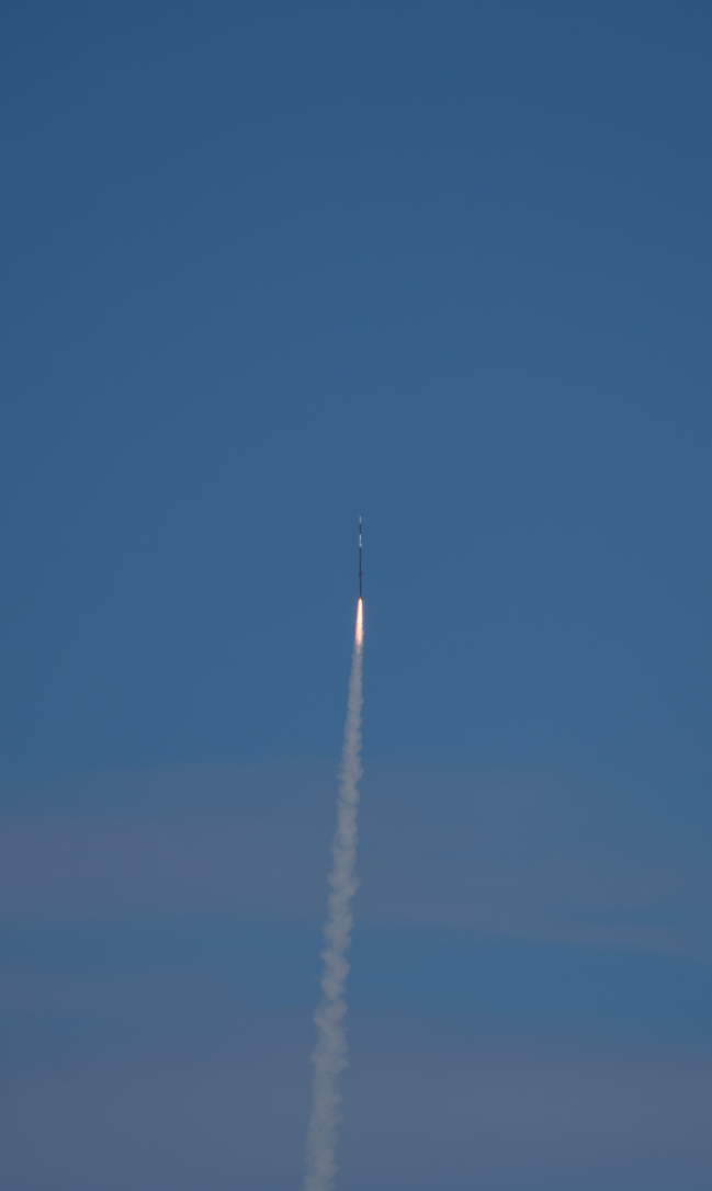 A rocket climbing into a blue sky, leaving a long exhaust trail