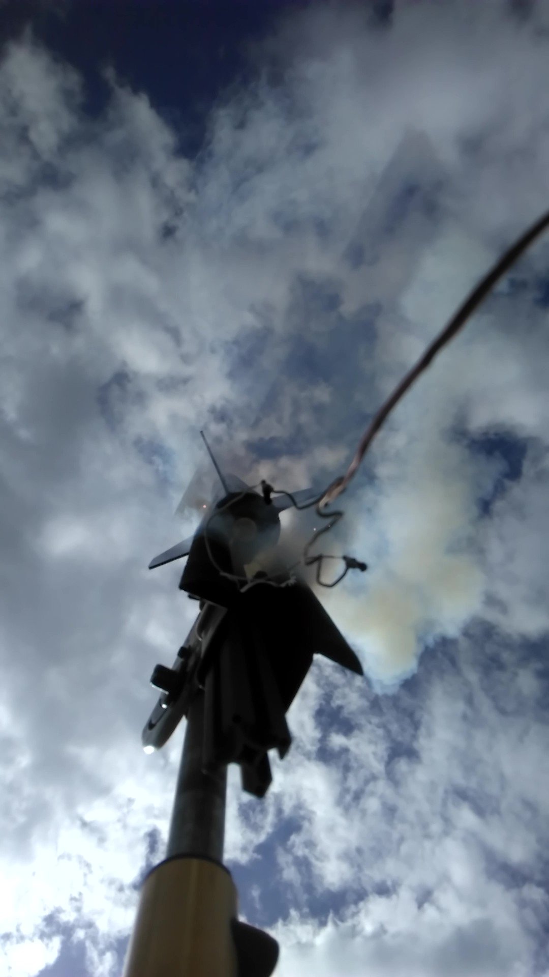 Looking up at a rocket on its launch rail beneath a cloudy sky