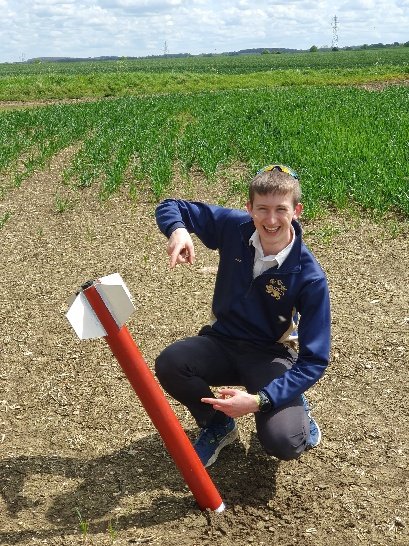 Daniel crouching beside a red rocket embedded nose-first in a field