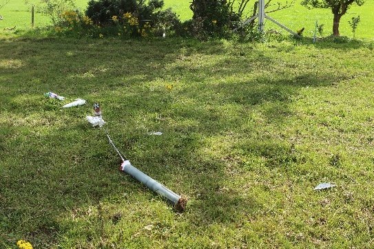 A damaged rocket body and scattered debris lying on grass