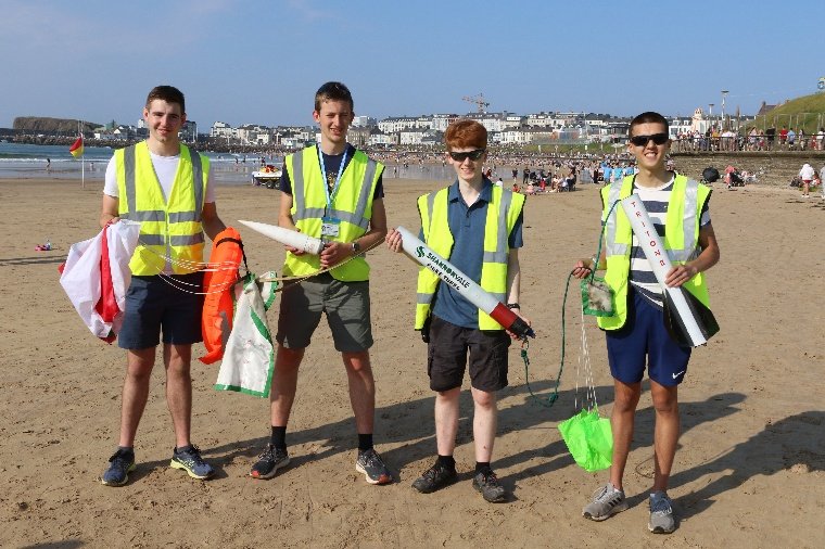 The four-person team on the beach holding the recovered rocket sections, parachutes and flotation equipment